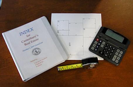 Binder titled "Index for Canterbury's Real Estate" next to floorplan, measuring tape, and a calculator
